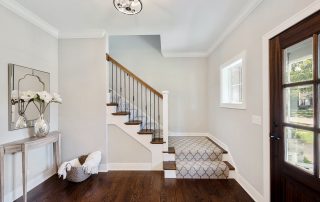 Cream-painted interior residential entryway with white ceiling, dark wood staircase, and dark wood entry door in Winchester