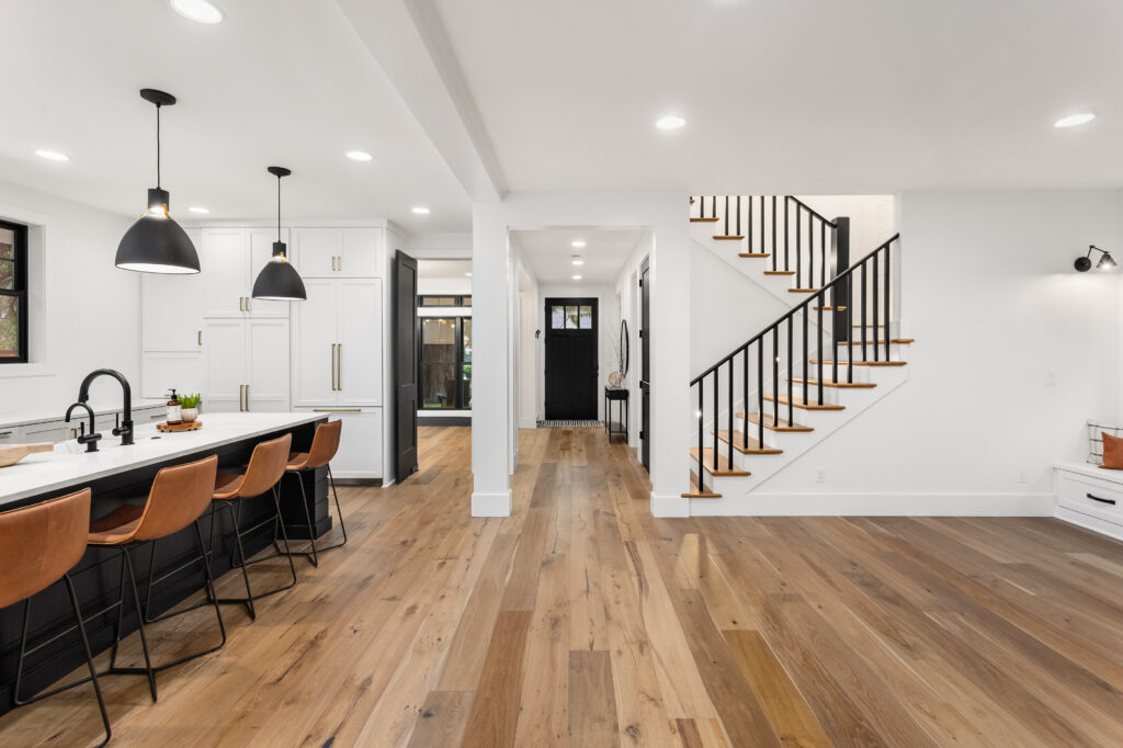 Kitchen and living room interior in new farmhouse style luxury home with open concept floor plan. Features large island with farmhouse sink, hardwood floors, and black accents. interior paint drying time between coats