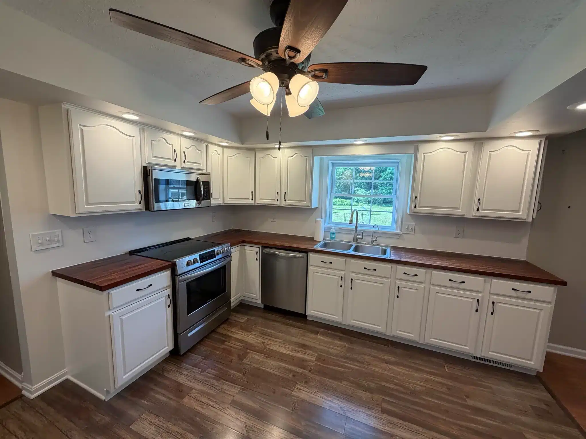 White Kitchen Cabinets Dark Wood Counters White-painted residential kitchen cabinets with dark wood countertops, stainless steel appliances, and brown wood flooring.