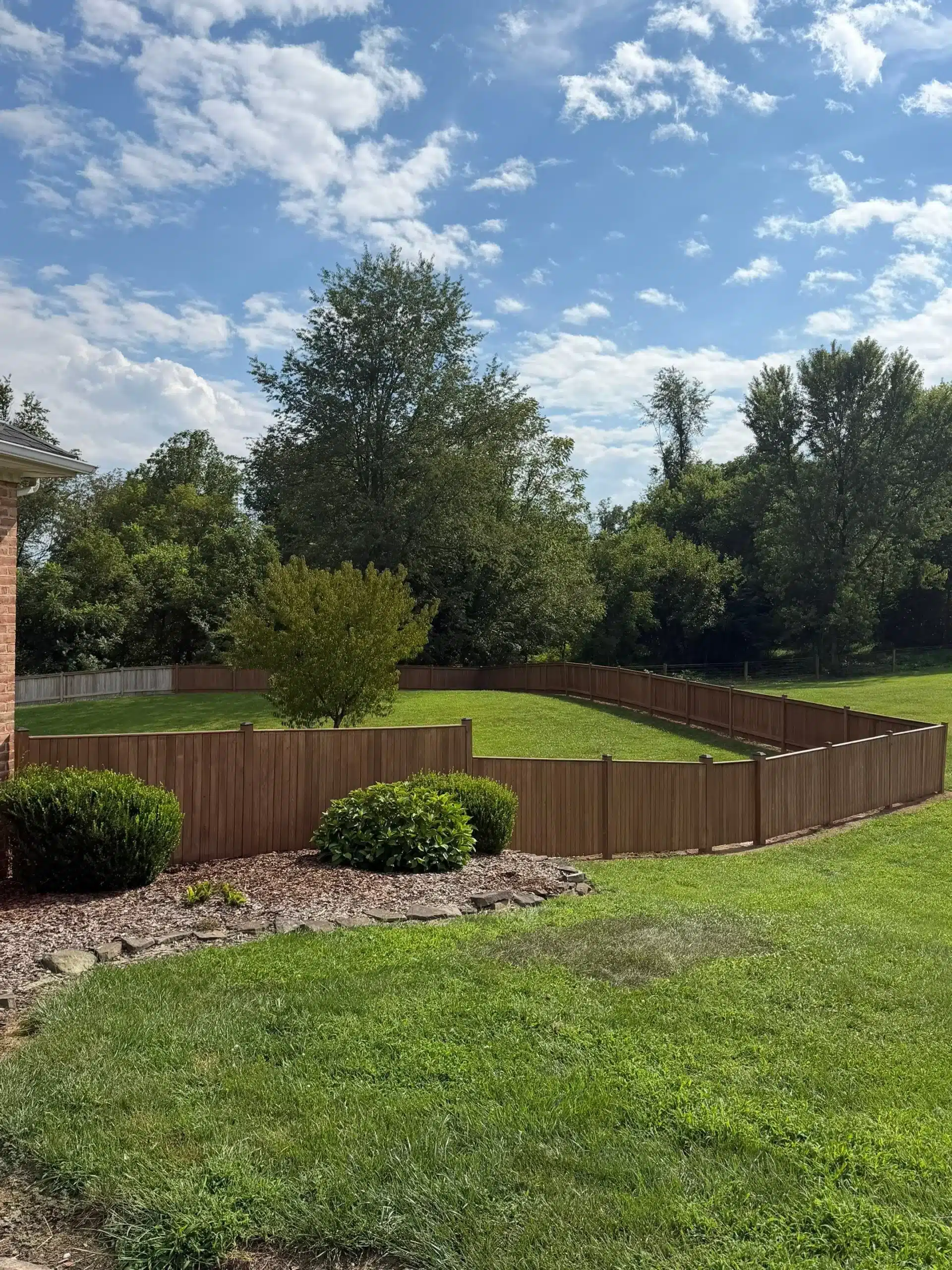 Brown Stained Residential Fence Brown-stained wooden residential fence enclosing backyard with green lawn and mature trees.