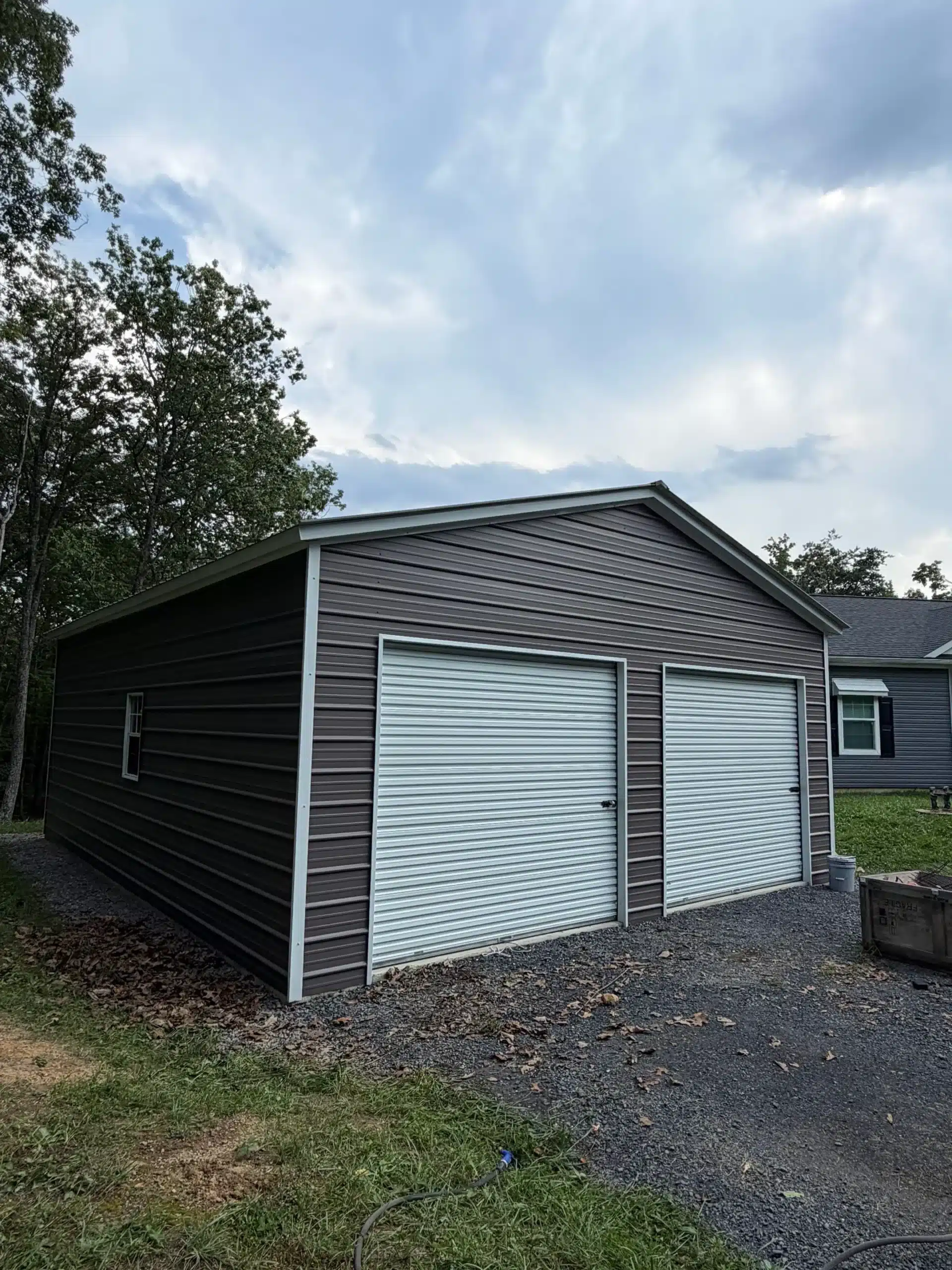 Black and Light Blue Metal Garage Black horizontal metal siding garage with light blue roll-up doors, white trim, and gravel driveway in Winchester, WV.